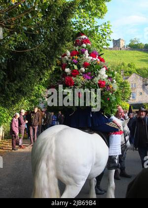 Il Castleton Garland King indossando un ghirlone di fiori cavalcate a cavallo all'antica cerimonia Castleton Garland 2022 con Peveril Castello in bg Foto Stock