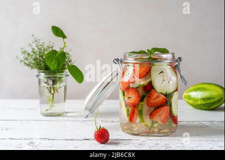 Acqua infusa in vaso di vetro fatto con fragola e meloncella che è ibrido di cetriolo e melone, timo, menta. Foto Stock