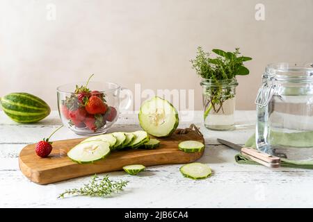 Preparazione di acqua infusa con fragola e meloncella che è ibrida di cetriolo e melone, timo, menta. Foto Stock