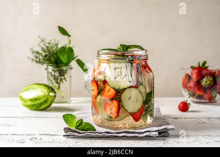 Acqua infusa in vaso di vetro con ingredienti - fragola, meloncella che è ibrido di cetriolo e melone, timo, menta. Foto Stock