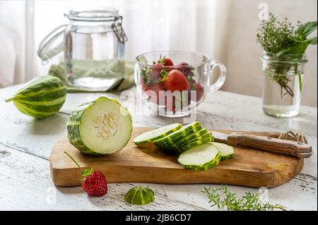 Preparazione di acqua infusa con fragola e meloncella che è ibrida di cetriolo e melone, timo, menta. Foto Stock