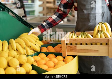 Mazzo di banane sulle scatole nel supermercato, un lavoratore di negozio di alimentari che mette banane mature in una scatola nella sezione frutta, shopping biologico Foto Stock