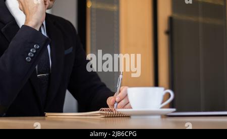 uomo d'affari in abito nero che lavora alla scrivania in ufficio Foto Stock