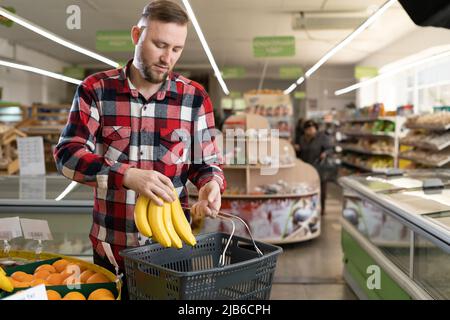 Negozi di alimentari. Uomo allegro in supermercato scelta di frutta fresca e verdure, portando cestino di acquisto di cibo naturale sano in negozio. Foto Stock