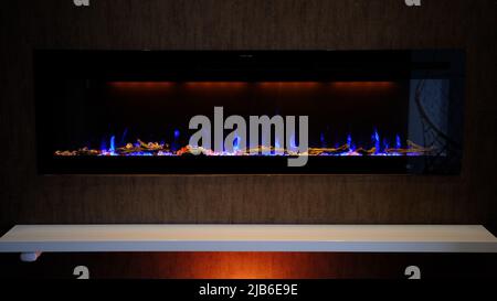 vista sul camino elettrico con fiamma artificiale scintillante, decorazione per l'interno, fiamma blu su cristalli con retroilluminazione arancione. Foto Stock