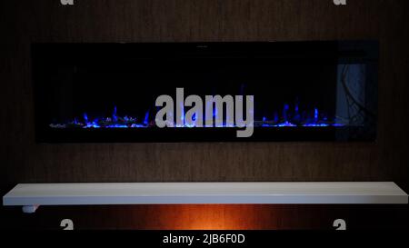 vista sul camino elettrico con fiamma artificiale scintillante, decorazione per l'interno, fiamma blu su cristalli con retroilluminazione arancione. Foto Stock