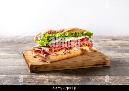 Sandwich sottomarino con prosciutto, formaggio, lattuga, pomodori, cipolla, mortadella e salsiccia su tavola di legno Foto Stock