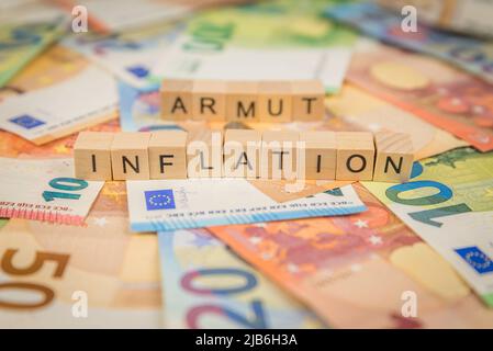 La parola inflazione e povertà - in tedesco per i poveri - sullo sfondo delle banconote banconote banconote banconote banconote in euro con testo scritto a cubo di legno Foto Stock