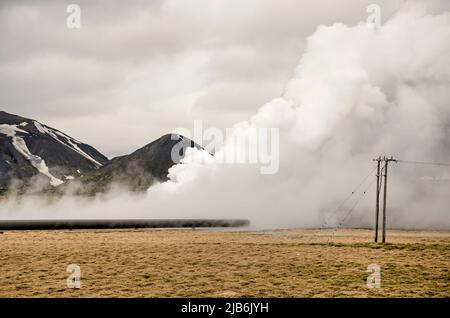 Hengill, Islanda, 22 aprile 2022: Vapore caldo che esce dal terreno in un paesaggio erboso con linee elettriche vicino al piano geotermico Hellisheiði Foto Stock
