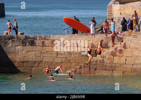 Nuoto in mare e paddleboard al largo delle mura del porto di Porthleven, Cornovaglia Foto Stock