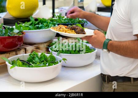 Un uomo sceglie un'insalata dal bar con insalata di erbe fresche al buffet dell'hotel. Cibo salutare Foto Stock