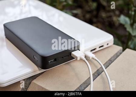 Power Bank ricarica un computer portatile tramite cavo USB di tipo C sulla strada. Primo piano, messa a fuoco selettiva Foto Stock