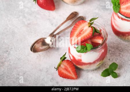 Cheesecake alla fragola. Cheesecake o trifle con fragola in vetro su sfondo vecchio tavolo grigio cemento. Cheesecake senza cottura. Dess Foto Stock