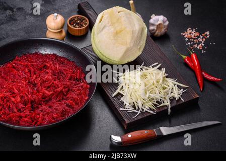 Barbabietole tritate in una padella, spezie ed erbe aromatiche su un tagliere di legno come ingredienti nella preparazione del tradizionale borscht ucraino Foto Stock