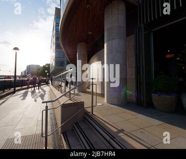 Londra, Greater London, Inghilterra, 21 2022 maggio: La luce serale splende sulla riva nord del Tamigi mentre i pedoni camminano lungo la passeggiata. Foto Stock