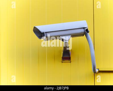 Telecamera CCTV sulla parete esterna testurizzata di colore giallo Foto Stock