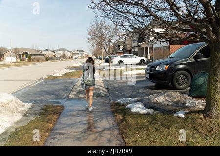 Una ragazza cammina lungo il marciapiede all'inizio della primavera in una giornata calda in Canada Foto Stock