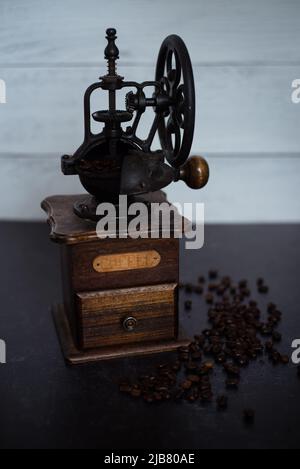 Macinacaffè vintage con chicchi su sfondo nero scuro e shiprap. Profondità di campo. Legno e ferro da stiro. Foto Stock