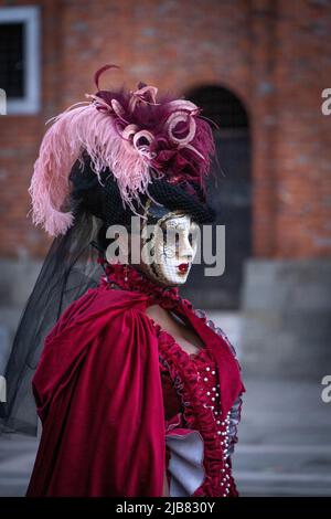 Venezia, Italia - 18.02.2022: Donna mascherata in abito rosso con piume rosa e viola al carnevale veneziano Foto Stock