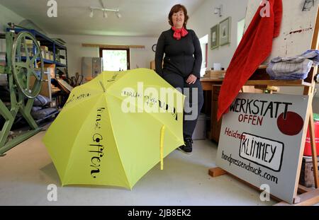 Rothen, Germania. 03rd giugno 2022. Heidrun Klimmey si trova nella sua officina presso Rothener Hof, dove realizza stampe. Un ombrello giallo con l'iscrizione 'Kunst offen' (Art Open) invita i visitatori a vedere il workshop e una mostra 'Zwischen uns' (tra noi) di cinque artisti femminili. Durante la campagna 'Art Open' a livello nazionale, circa 900 artisti in più di 500 località apriranno i loro laboratori e studi ai visitatori nel weekend di Whitsun del 4-6 giugno 2022. Credit: Bernd Wüstneck/dpa/Alamy Live News Foto Stock