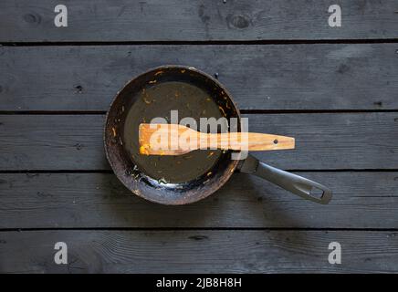 una padella con gli avanzi di cibo e una spatola di legno dopo la frittura è sul tavolo in cucina, una padella sporca è sul tavolo Foto Stock