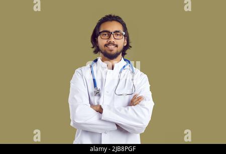 Ritratto del giovane medico indiano in cappotto bianco con stetoscopio in piedi con le braccia ripiegate Foto Stock