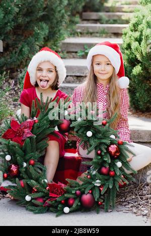 Buon Natale. Ritratto di due ragazze divertenti felici a Santa Hat con la corona di Natale. Buone feste. Magia delle fate. I bambini sono felici di godersi una vacanza. Natale nel mese di luglio Foto Stock