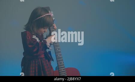 La bambina in un abito vintage suona una chitarra acustica come un contrabbasso Foto Stock