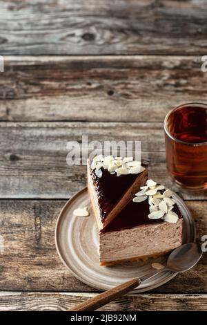 Due fette di cheesecake al cioccolato con petali di mandorle, con una tazza di tè su sfondo di legno. Spazio di copia. Composizione verticale con spazio di copia Foto Stock