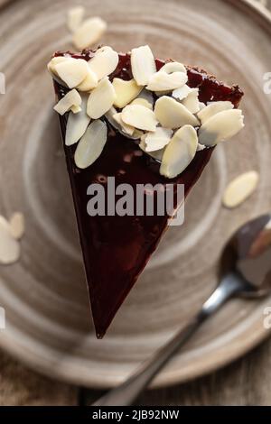 Fetta di cheesecake al cioccolato con petali di mandorle che si guarnisce su un piatto di ceramica con cucchiaio. Vista dall'alto. Primo piano. Menu dolciario, ricetta. Orientatio verticale Foto Stock