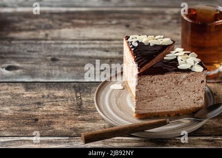 Due fette di cheesecake al cioccolato con petali di mandorle, con una tazza di tè su sfondo di legno. Spazio di copia. Composizione orisontale sul sid destro Foto Stock