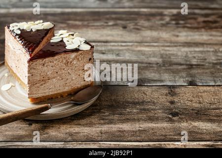 Due fette di cheesecake al cioccolato con petali di mandorle su sfondo di legno. Composizione orisontale sul lato sinistro della cornice. Spazio di copia Foto Stock