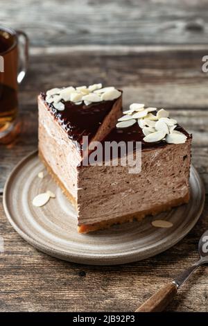 Due fette di cheesecake al cioccolato con petali di mandorle che si condiscono con una tazza di tè su sfondo di legno. Orientamento verticale, primo piano Foto Stock