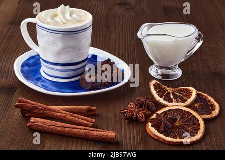 Tazza blu di caffè con crema, cioccolato, latte e spezie su un tavolo di legno scuro Foto Stock