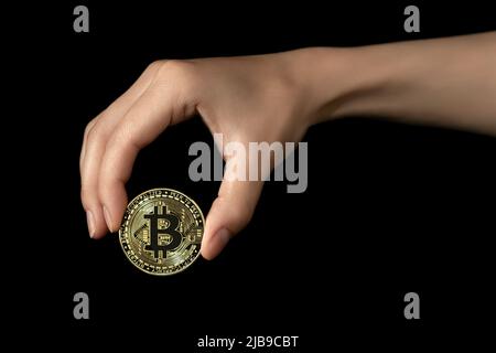 La mano della donna tiene un bitcoin nelle sue dita. Isolato su sfondo nero. Foto Stock