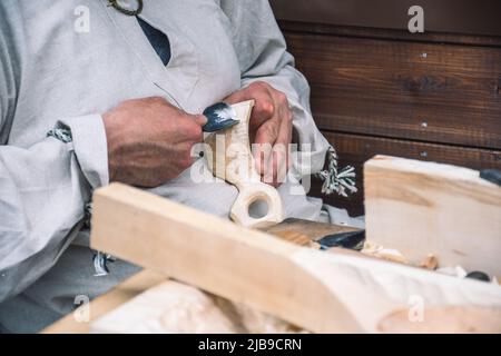 Artigiano lituano in costumi tradizionali intagliando una tazza di legno e vendendo i suoi manufatti e oggetti in legno fatti a mano in un mercato locale di strada Foto Stock