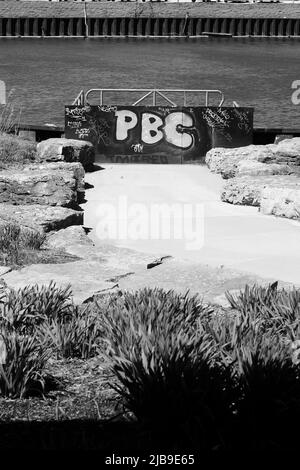 Le lettere PBC spruzzano dipinto su una parete di fronte al mare in bianco e nero. Foto Stock
