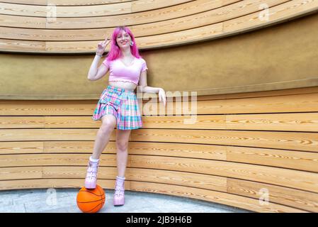 primo piano ritratto di donna alternativa con i capelli rosa appesi fuori agghiacciante e sorridente in piedi isolato contro la moderna parete di legno sfondo. happines Foto Stock