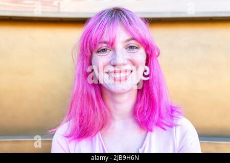 primo piano ritratto di donna alternativa con capelli rosa appesi fuori agghiacciante e sorridente in piedi isolato contro la moderna parete di legno sfondo. happines Foto Stock