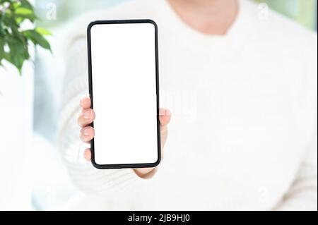 Cellulare mockup. Donna in abiti bianchi mostra bianco cellulare schermo bianco bianco. Donna mano che tiene e mostra nero cellulare smart telefono cellulare con bianco bianco vuoto Foto Stock