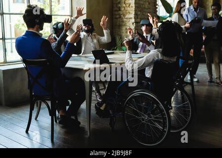 Diversi uomini d'affari che lavorano con cuffie per realtà virtuale all'interno dell'ufficio di colleghi - concentrarsi sulla donna africana seduta su sedia a rotelle Foto Stock
