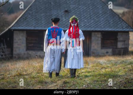 Una coppia vestita in costume tradizionale folk. Costume slovacco in autunno natura. Vecchio cottage di campagna sullo sfondo. Giovane coppia in costume folk wal Foto Stock