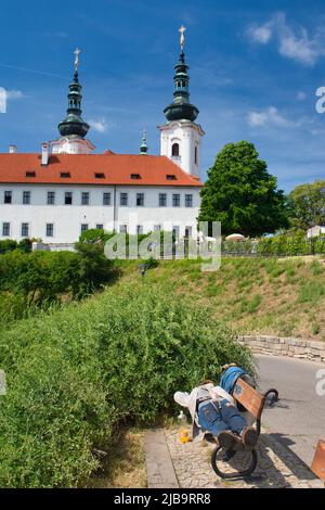 Dormendo senzatetto su una panchina, monastero Strahov in background. Foto Stock