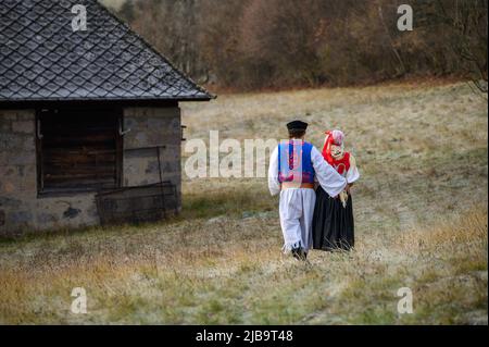 Una coppia vestita in costume tradizionale folk. Costume slovacco in autunno natura. Vecchio cottage di campagna sullo sfondo. Giovane coppia in costume folk wal Foto Stock