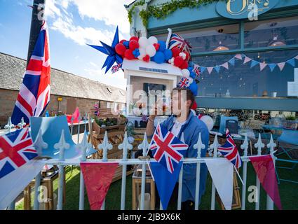 Ballater, Scozia, Regno Unito. 4 giugno 2022. La celebrazione del Giubileo del platino della Regina si celebra nel villaggio di Ballater, vicino a Balmoral, sul Royal Deeside, nell'Aberdeenshire. PIC; Adam, il proprietario dell'azienda termale di Aberdeen, Hairy Hoosewife, gode di un drink circondato da bandiere dell'Unione sul suo stalla. Iain Masterton/Alamy Live News Foto Stock