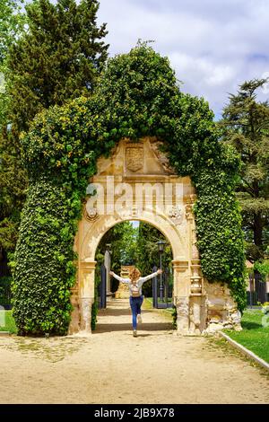 Donna che salta felicemente mentre passa attraverso un arco di pietra in un parco pubblico della città. Foto Stock