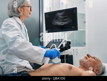 Esame ecografico del cuore per l'uomo anziano con ecografo durante l'esame medico. Esame di salute del cuore con macchina di scansione a ultrasuoni Foto Stock