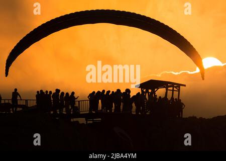 Persone che guardano l'atleta del parapendio sopra una montagna e tramonto vista. Foto Stock