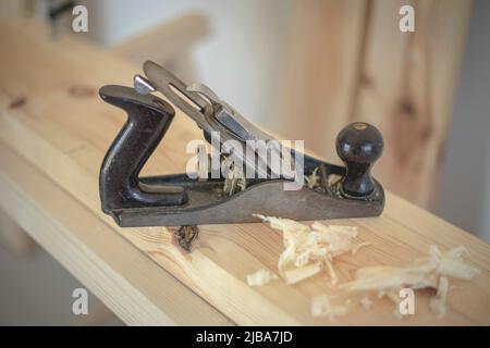 Primo piano di una vecchia e tradizionale piallatrice in legno metallico nero su asse di legno in un negozio di carpenteria con luce naturale Foto Stock