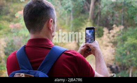 Uomo viaggiatore blogger con zaino in natura filma video su smartphone fotocamera Foto Stock